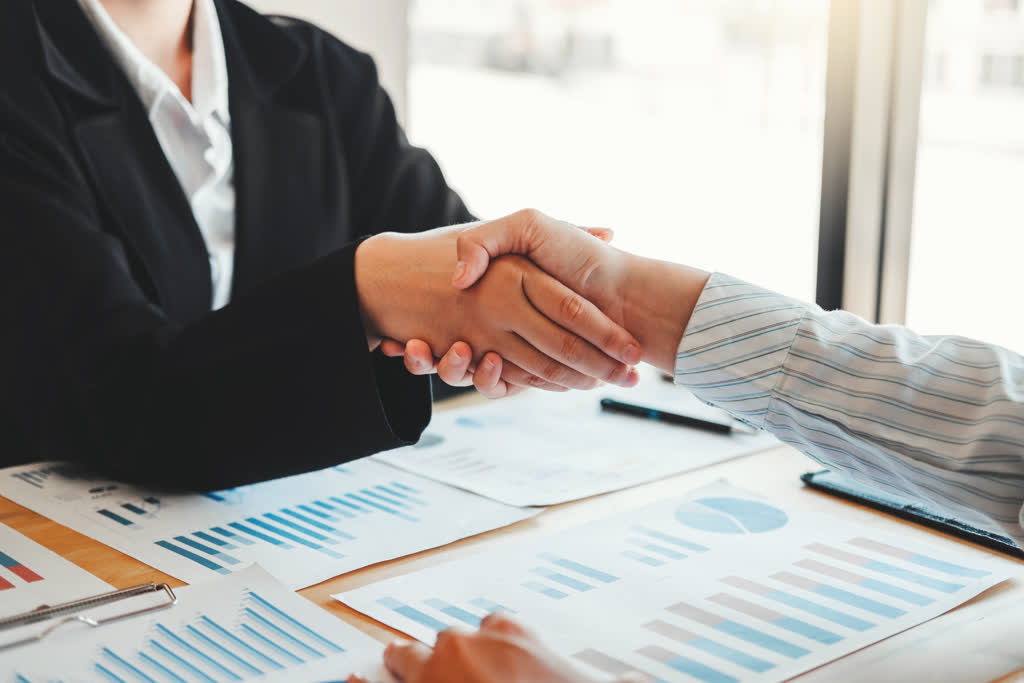 Shaking hands over various analytical charts.